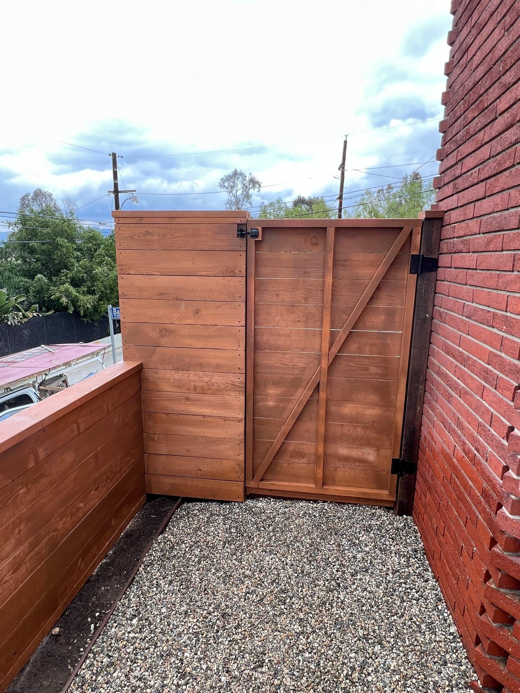 Redwood gate with Z-brace and black hardware next to a brick wall