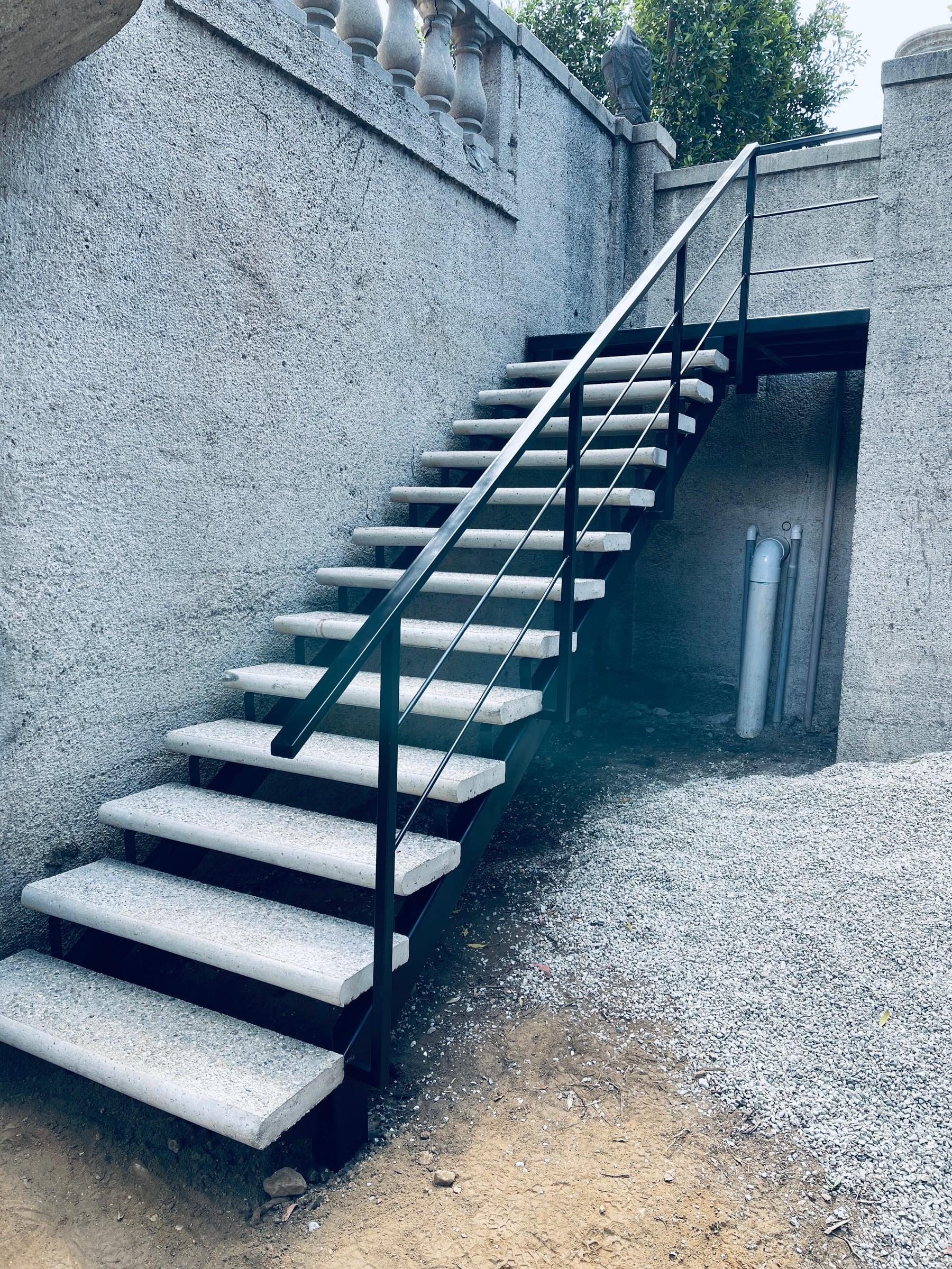 Custom iron staircase railing with concrete-clad steps leading to a raised patio