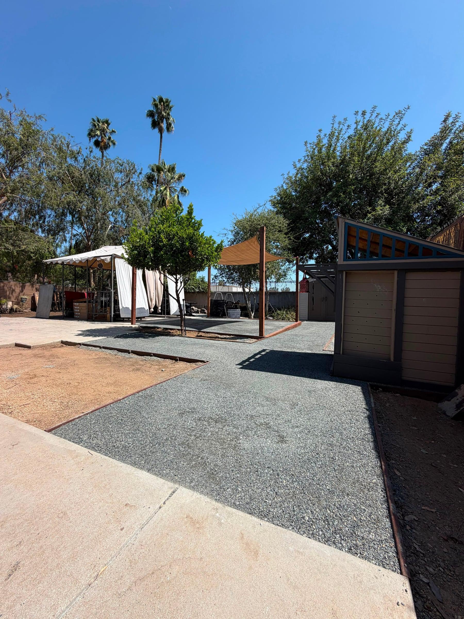 Backyard gravel patio with a shade sail and citrus tree